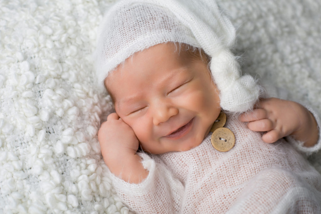 Smiling newborn on a white blanket.